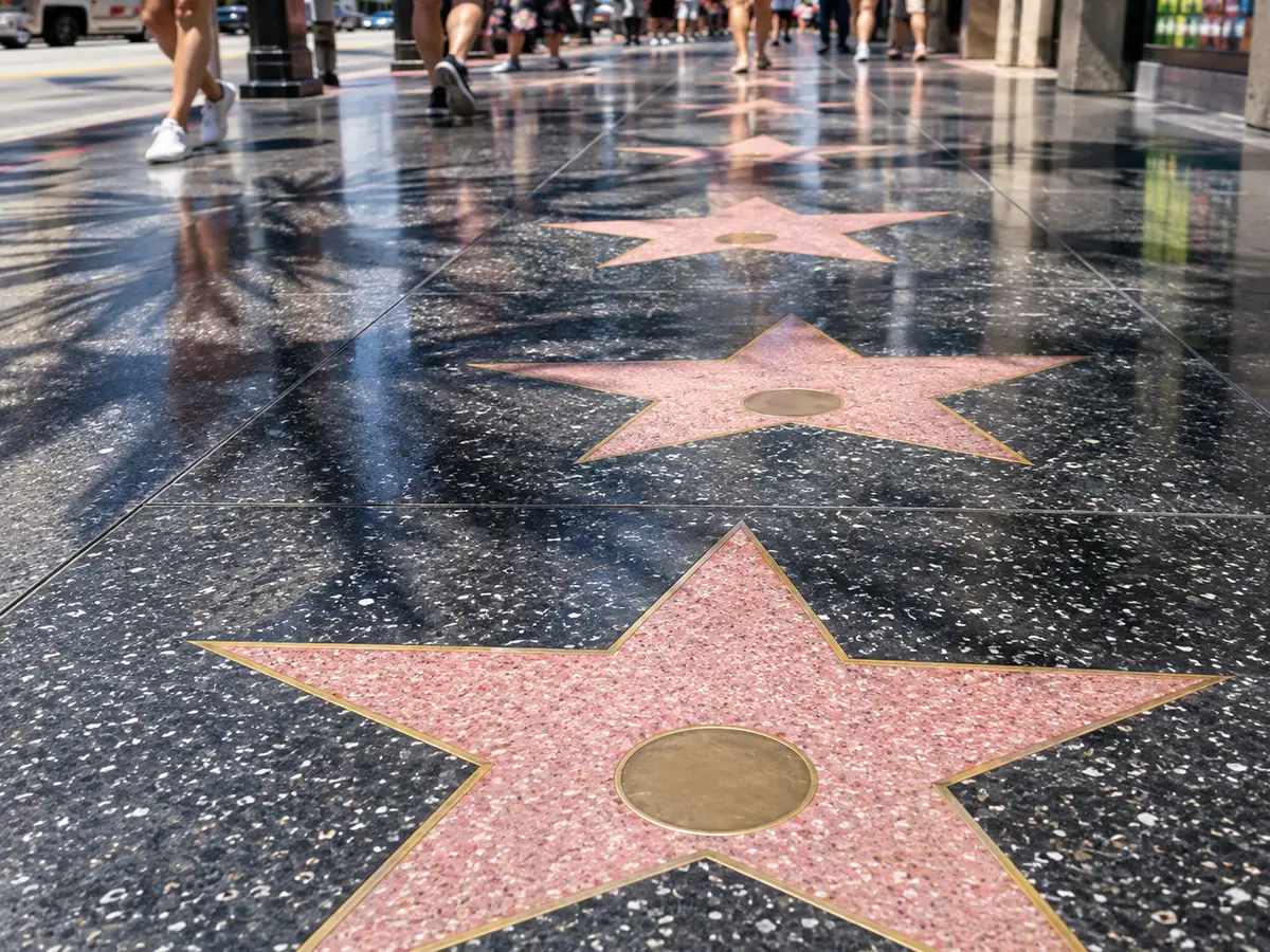 Des étoiles en terrazzo rose aux bordures en laiton incrustées dans un trottoir sombre à Hollywood